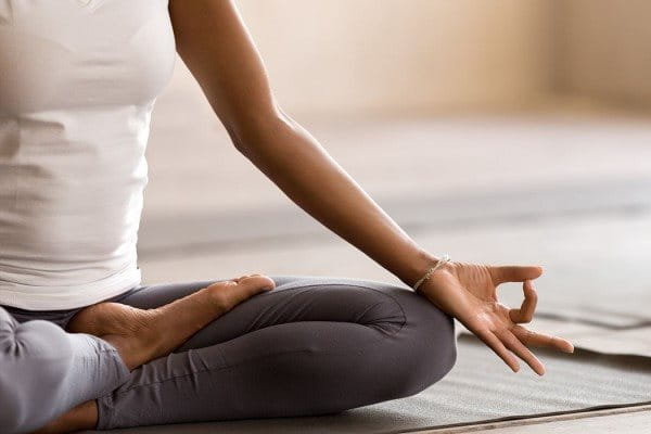 Ansicht von halbem Oberkörper und Beinen einer Frau, die ihm Lotussitz auf einer Yogamatte sitzt. 