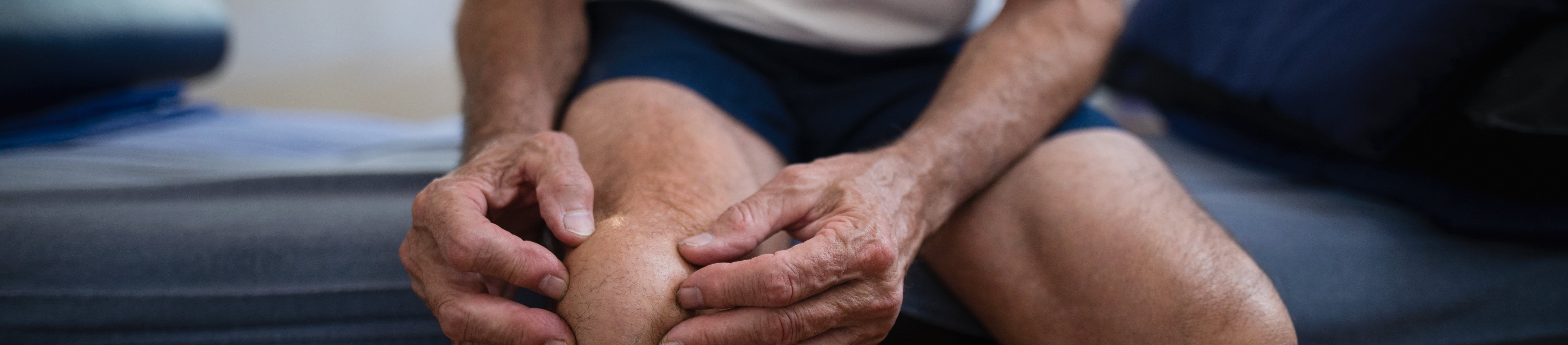 Male patient sitting holding knee in pain.