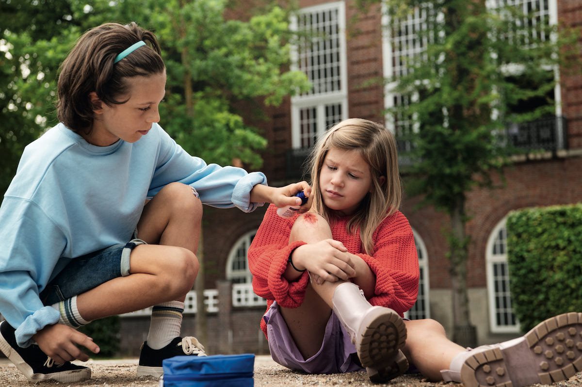 Een meisje zorgt voor een ander meisje met een geschaafde knie