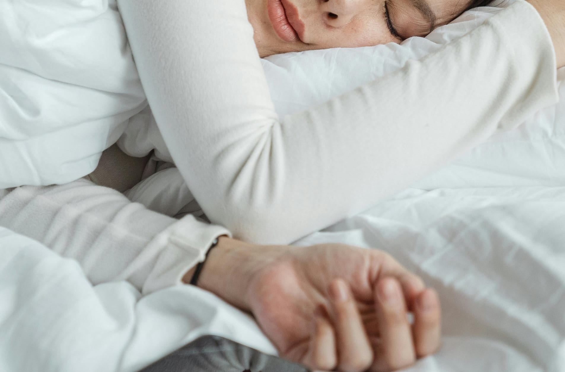 Frau liegt ruhig schlafend in einem Bett mit heller Bettwäsche.