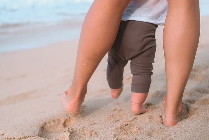 Die Beine eines Erwachsenen und eines Kindes am Strand