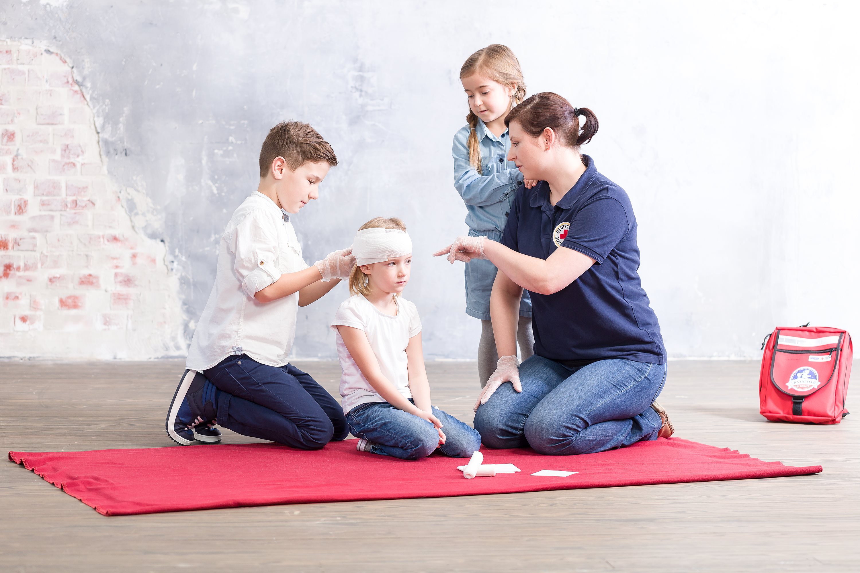 Een medewerker van het Rode Kruis laat een groep kinderen in een klas zien hoe ze een hoofdverband moeten aanbrengen