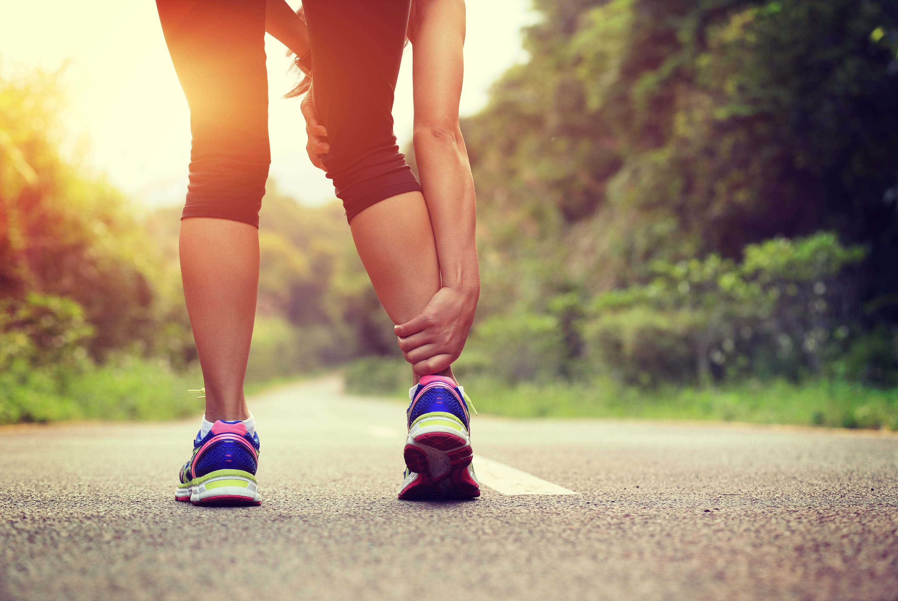 Eine Frau beim Joggen, die sich ihr schmerzendes Bein hält.