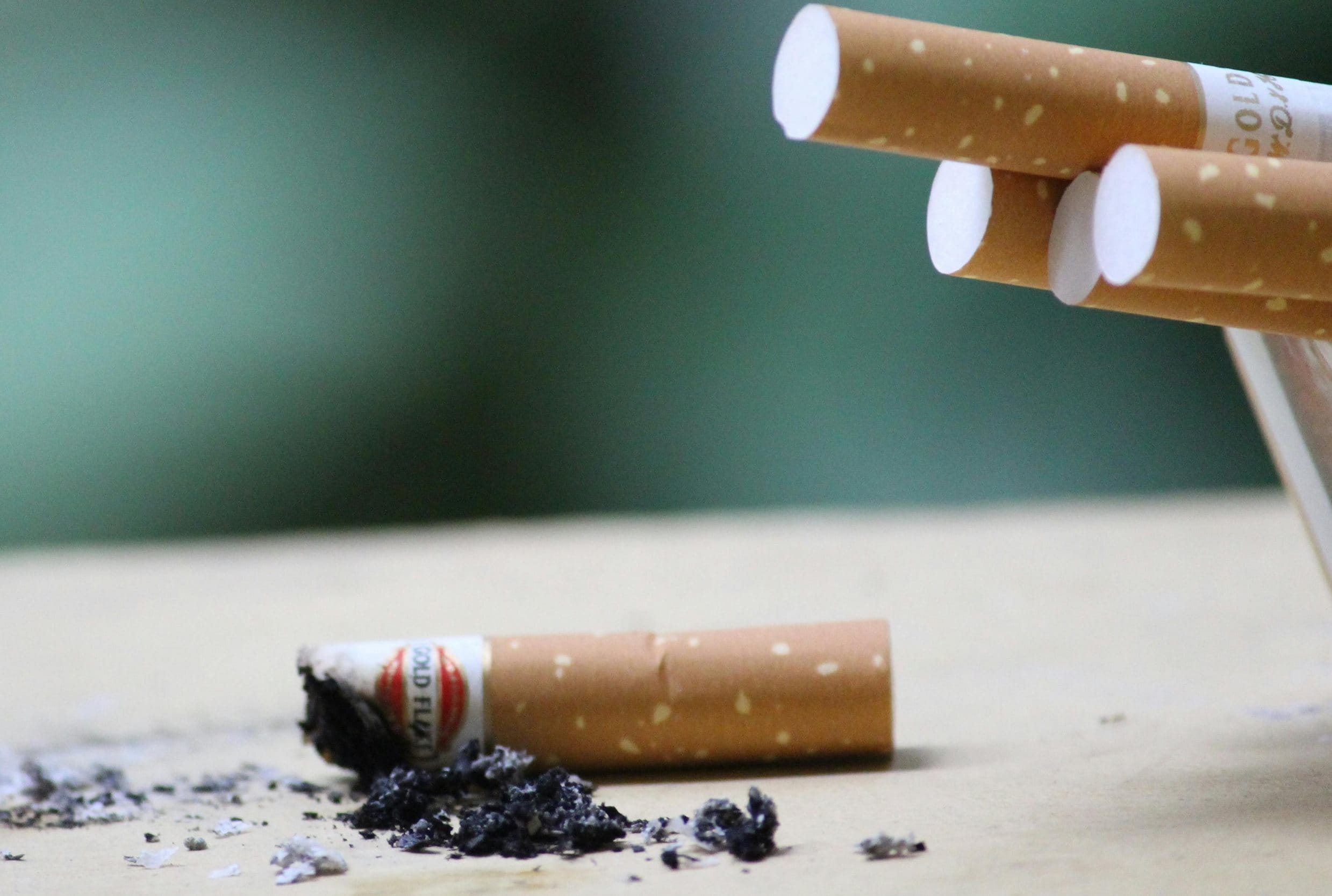 Nahaufnahme eines vollen Aschenbechers, neben dem eine abgebrannte Zigarette liegt.