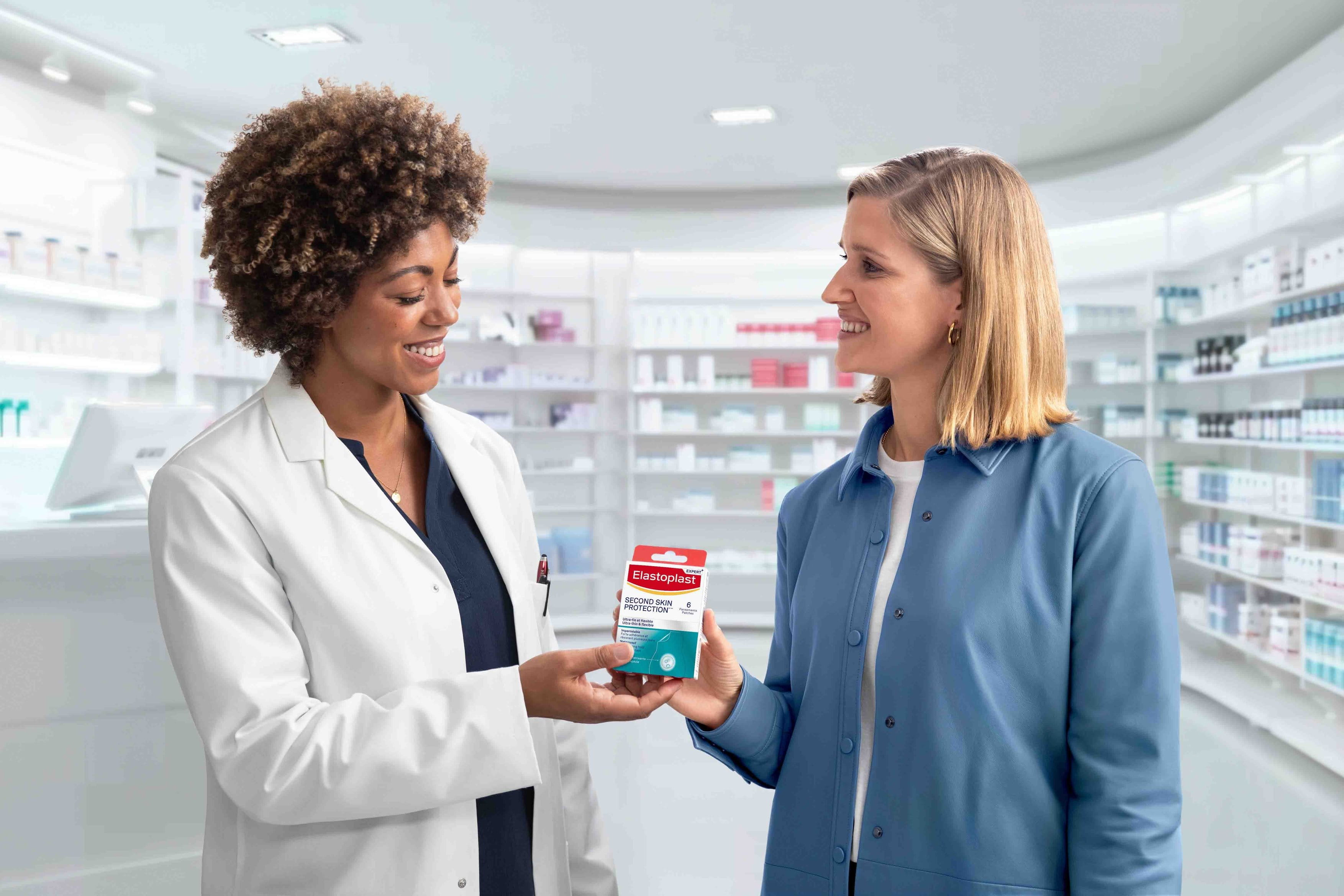 A pharmacist in a pharmacy that specializes in wound care gives a happy customer a pack of Elastoplast Second Skin Protection plasters.