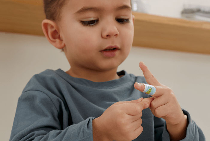 Ein Kind schaut auf seinen Finger, an dem ein buntes Pflaster klebt.