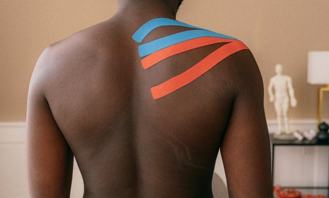 Mann mit orangenem und blauem Kinesiologie Tape am Schulterblatt.