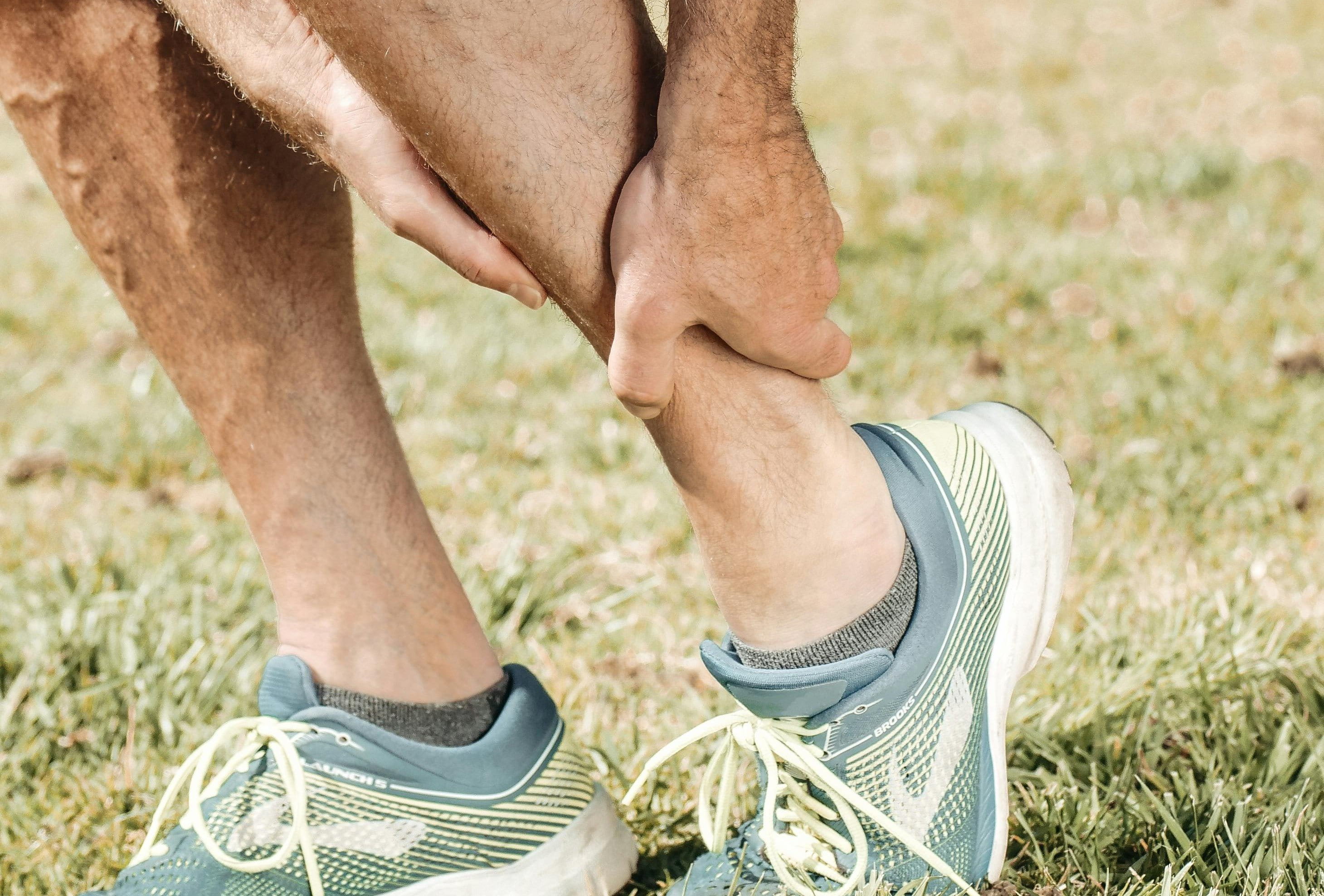 Ein Mann in Laufschuhen hält sich seinen Knöchel zur Stabilisierung.