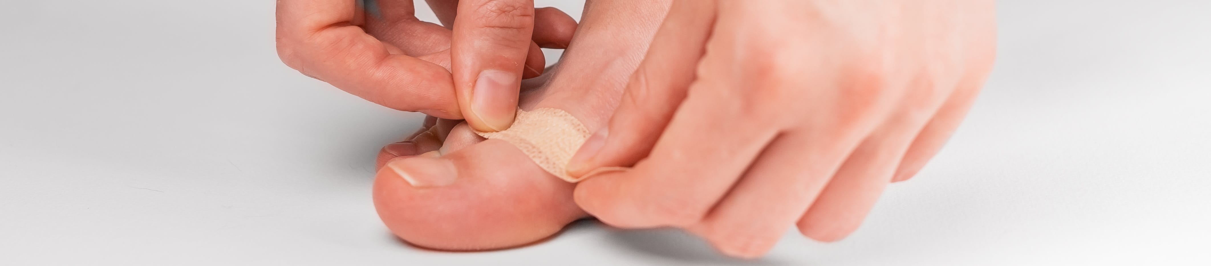 Nahaufnahme, wie eine Frau ein Pflaster auf den Fuss auflegt.