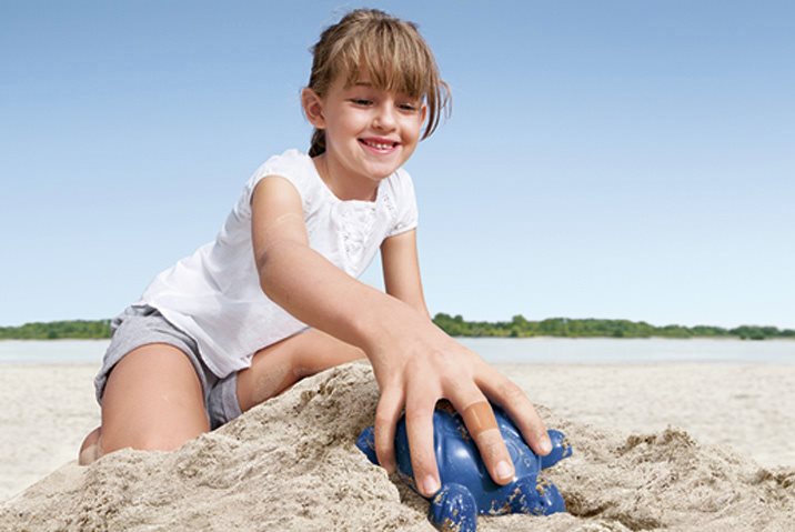 A young girl on a yellow tricycle smiles as she skids across a gravel path